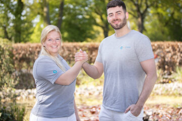 Zwei Pflegefreunde schlagen ihre Hände ein und lächeln dabei in die Kamera