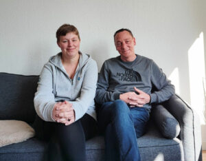 Sonja und Stefan sitzen auf einem Sofa und lächeln in die Kamera