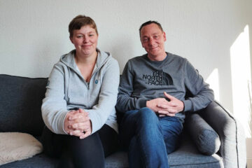 Sonja und Stefan sitzen auf einem Sofa und lächeln in die Kamera
