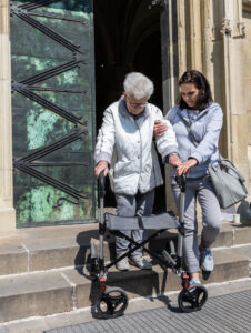 Pflegekraft unterstützt Patientin am Rollator beim Treppensteigen