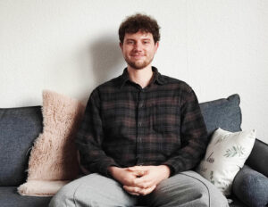 Benedict sitzt auf dem Sofa und lächelt in die Kamera