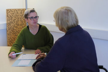 Pflegeberaterin Nicole Hülskötter im Gespräch mit einer Patientin. Vor ihnen liegt eine Mappe mit dem Pflegevertrag.
