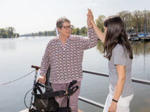 Patientin am Rollator und Pflegekraft geben sich High-Five vor dem Aasee