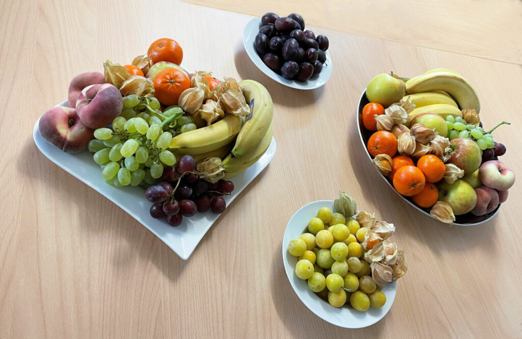 Vier Teller voller Obst. Von Banane, über Pflaumen, Mandarinen, Weintrauben, Pfirsiche bis hin zu Äpfeln und Physalis.