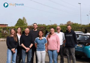 Die 7 Teilnehmer und Dozent Herr vom Kolke stehen auf dem Parkplatz der Pflegefreunde. Im Hintergrund sind die Autos der Pflegefreunde zu sehen