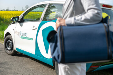 Pflegekraft mit blauer Wundtasche steht vor dem Pflegefreunde-Auto