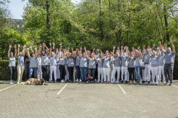 Das ganze Team der Pflegefreunde steht draußen und jubelt. Halten die Hände hoch