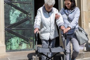 Pflegekraft unterstützt Patientin am Rollator beim Treppensteigen