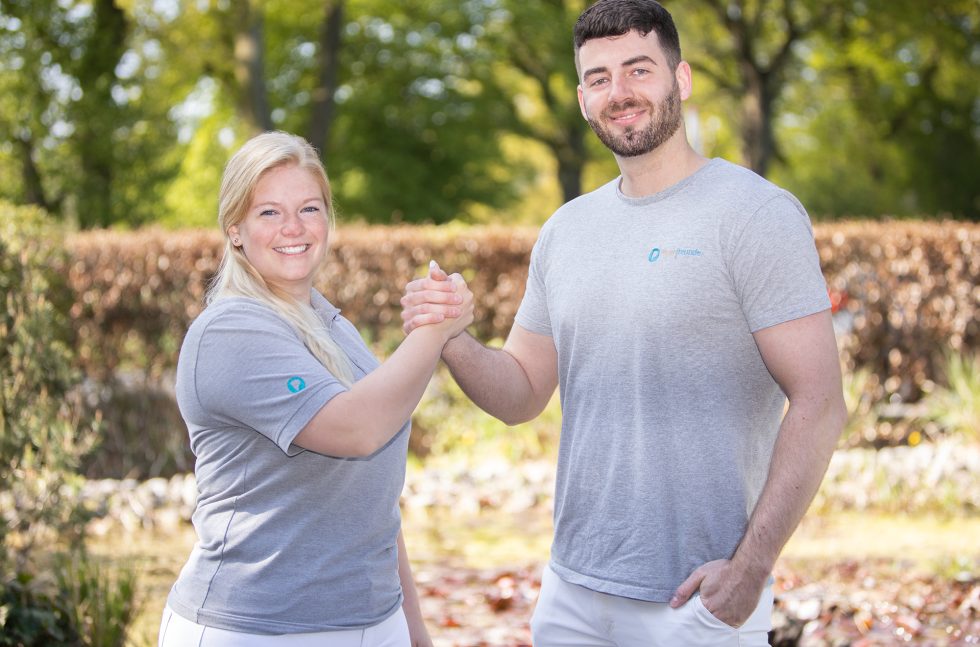 Zwei Pflegefreunde schlagen ihre Hände ein und lächeln dabei in die Kamera