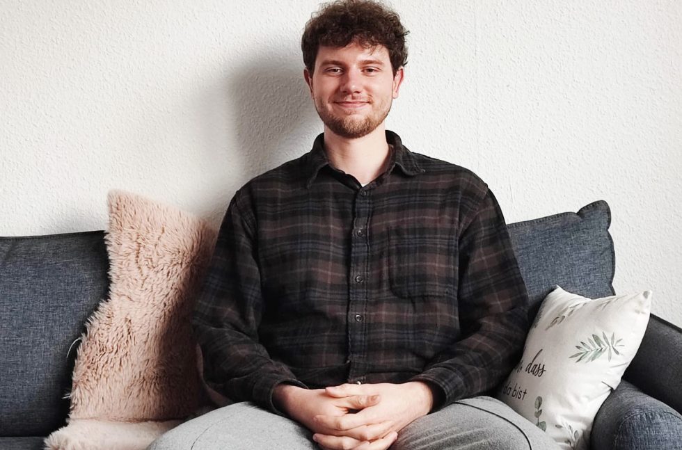 Benedict sitzt auf dem Sofa und lächelt in die Kamera