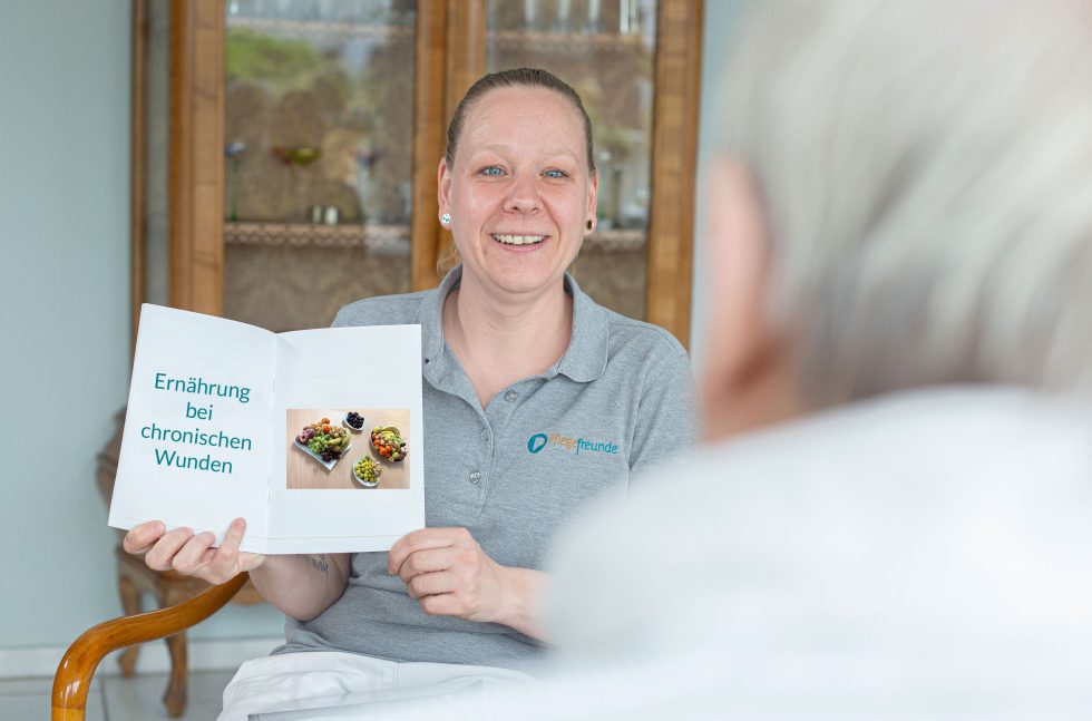 Wundexpertin sitzt Patienten gegenüber und hält Broschüre hoch. Da drin steht: Ernährung bei chronischen Wunden