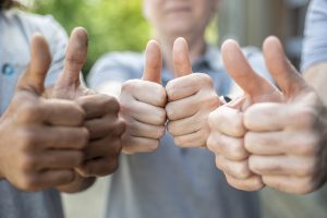 Drei Pflegefreunde halten mit ihren Händen den Daumen hoch in die Kamera