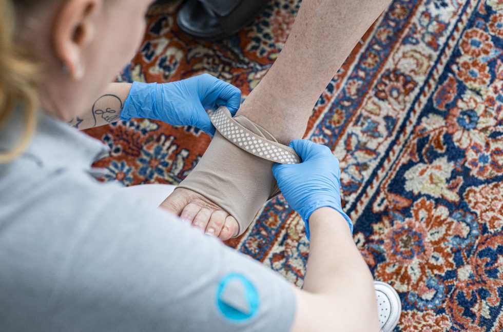 Pflegekraft zieht dem Patienten einen Kompressionstrumpf an