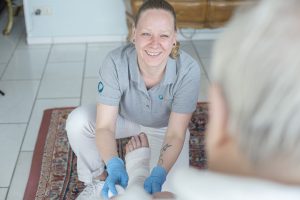 Pflegekraft versorgt den Verband am Bein des Patienten und schaut ihn dabei an.
