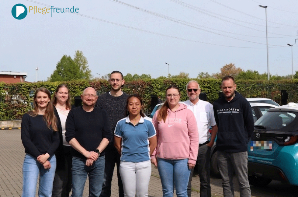 Die 7 Teilnehmer und Dozent Herr vom Kolke stehen auf dem Parkplatz der Pflegefreunde. Im Hintergrund sind die Autos der Pflegefreunde zu sehen